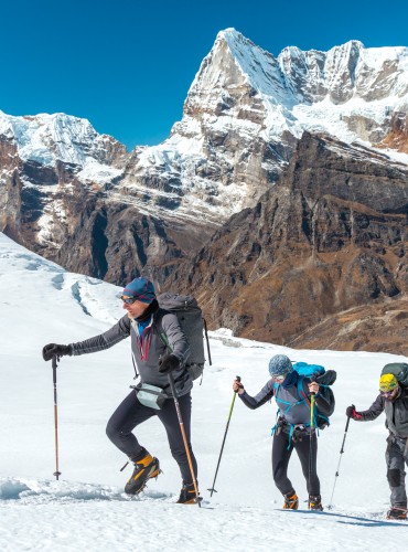 Adventurous People of variety of Age Origin and Ethnicity making Climb in high Altitude Mountains walking on Glacier with heavy Snow using trekking Poles and other Gear