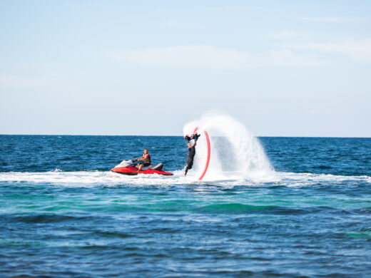 A rider on a flyboard in the ocean does difficult stunts.