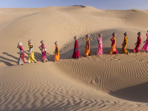 Women bear the responsibility of fetching water from the sparse wells within Rajasthan's vast Thar Desert. Trekking up the side of a sand dune, women expertly balance large clay water vessels atop their heads. Rajasthan, India