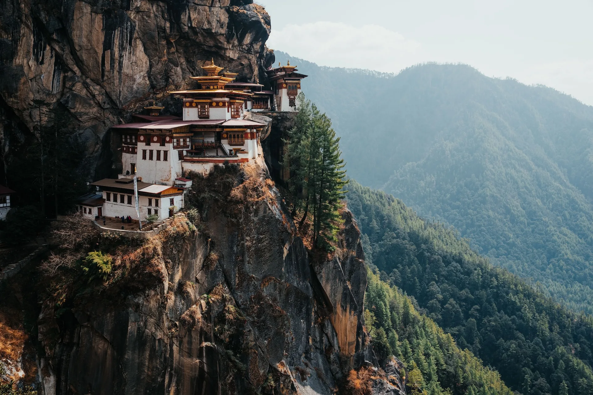 The iconic Tiger's Nest Monastery perched on a cliff in Bhutan, surrounded by lush green mountains under a clear sky.